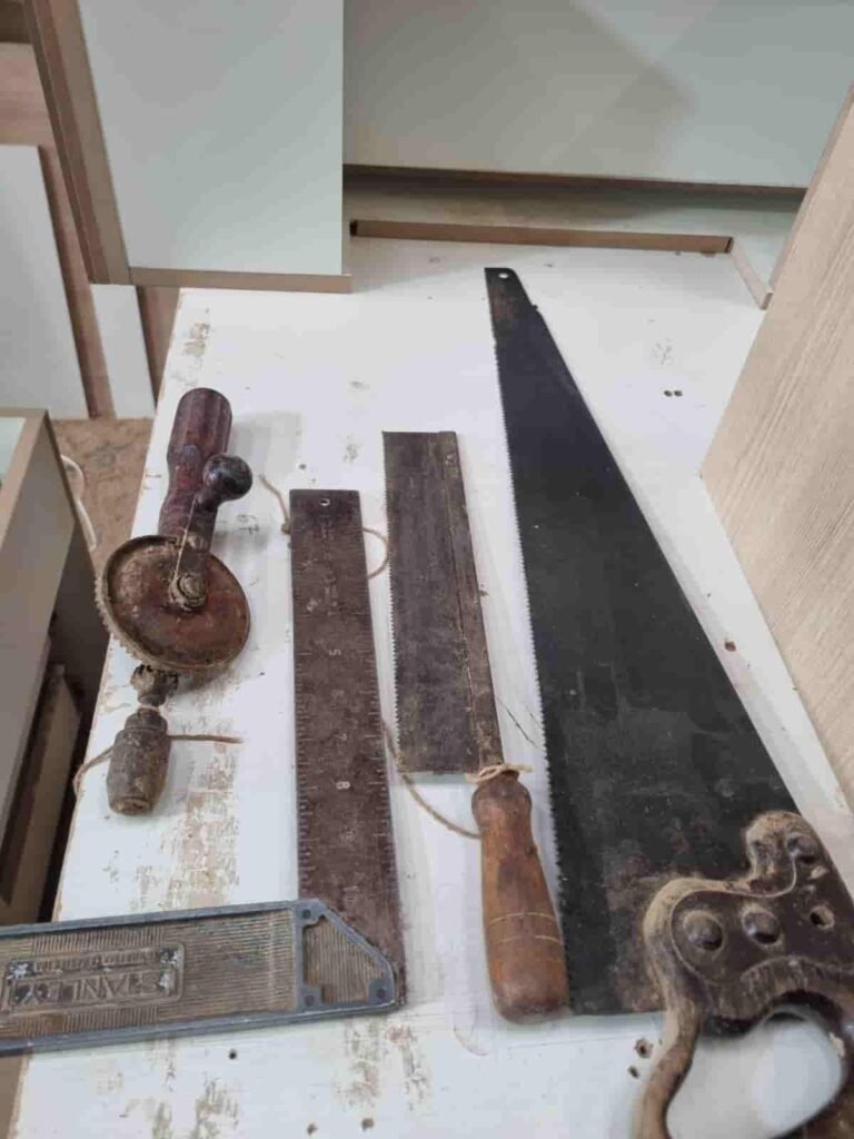Four antique 100-year-old woodworking hand tools including a vintage Stanley square and hand saws on a workshop bench.